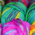 Brightly colored wool in greens, pinks, and yellows are tightly packed, showcasing vibrant colours and textures, conveying a lively, creative atmosphere.