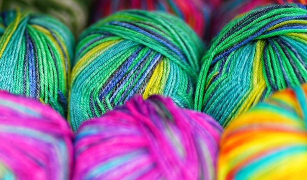 Brightly colored wool in greens, pinks, and yellows are tightly packed, showcasing vibrant colours and textures, conveying a lively, creative atmosphere.