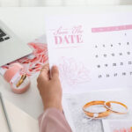An elegant image, with soft pink colours, featuring a laptop, calendar, notebook and pen.
