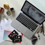 A wooden table displaying a laptop, sketchbook, and various drawing materials in a creative workspace.
