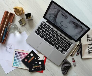 A wooden table displaying a laptop, sketchbook, and various drawing materials in a creative workspace.