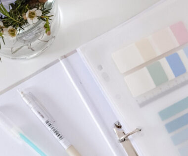 A notebook with a pen and pencils, vase of vibrant flowers on a desk.