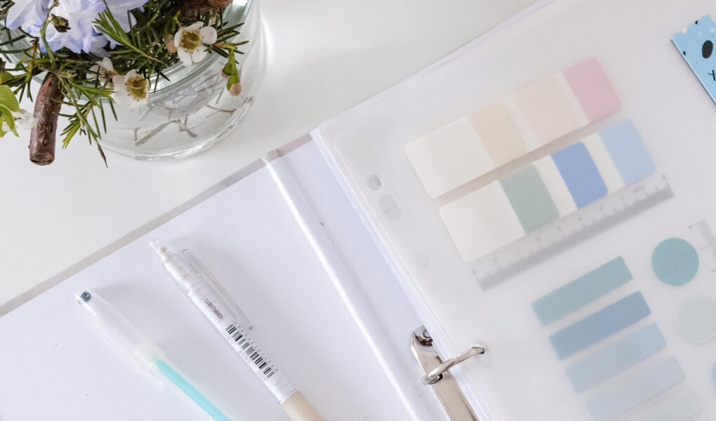 A notebook with a pen and pencils, vase of vibrant flowers on a desk.