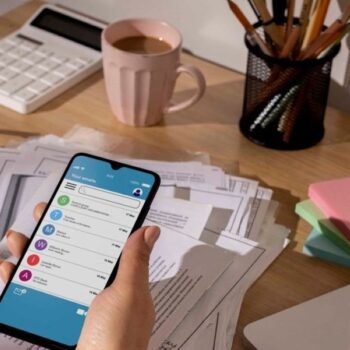 Workspace with a laptop and coffee cup and a items illustrating a visual guide on how to manage finances through smartphone mobile apps, featuring an app with budgeting tools.