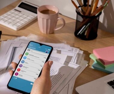 Workspace with a laptop and coffee cup and a items illustrating a visual guide on how to manage finances through smartphone mobile apps, featuring an app with budgeting tools.