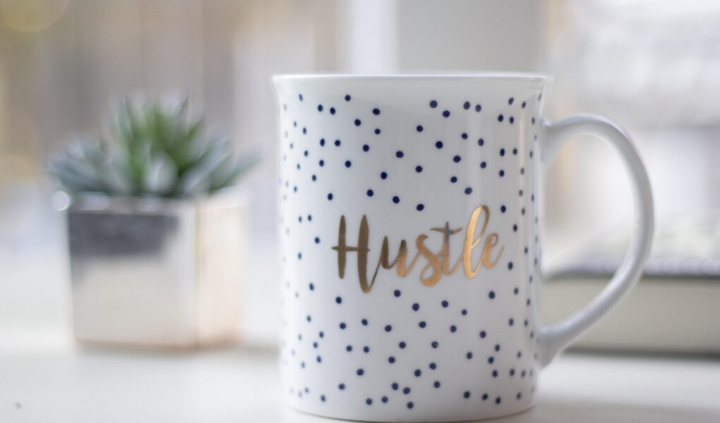 A stylish mug featuring the word "Hustle" in a gold font, ideal for coffee lovers and motivated individuals including those work on a freelance basis.