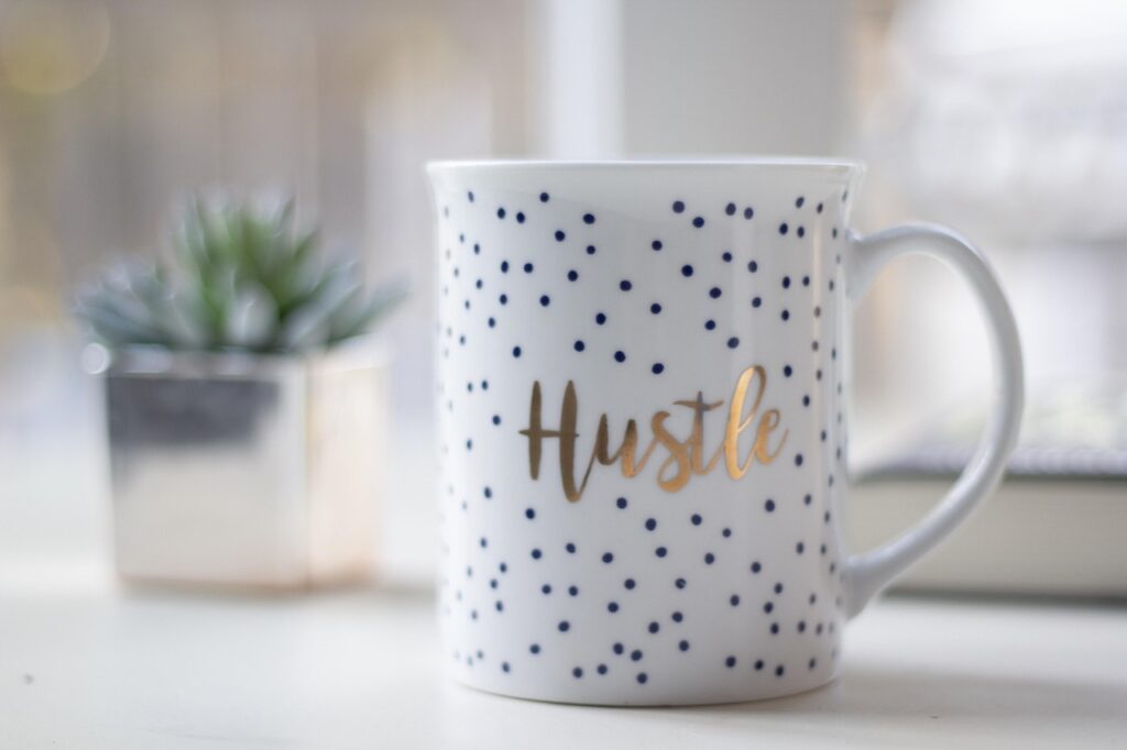 A stylish mug featuring the word "Hustle" in a gold font, ideal for coffee lovers and motivated individuals including those work on a freelance basis.